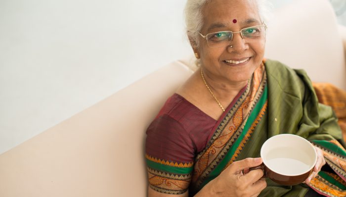 Smiling aged woman in traditiona Indian sari resting with a cup of tea, view from above